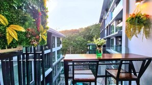 A balcony with a glass railing, a wooden table, and chairs. - B305 - 1 Bedroom Serviced Apartment Pool View near Ao Nang Beach (Tambon Ao Nang)