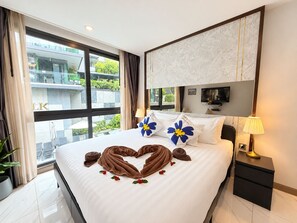 A hotel room with a bed, a TV, a nightstand, and a view of a building outside.