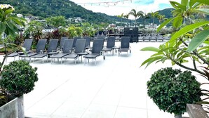 Une terrasse sur le toit, agrémentée de rangées de chaises longues, entourée de plantes en pot et offrant une vue sur un paysage montagneux.