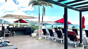 Une terrasse extérieure avec des chaises longues, des parasols et un espace barbecue.
