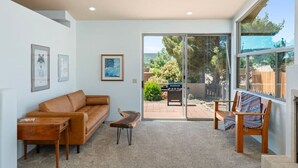 A living room with a sofa, coffee table, and chairs, a fireplace, and a sliding glass door leading to a patio with a barbecue grill.