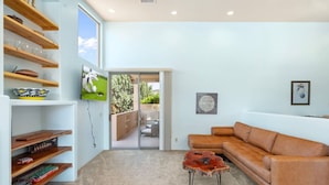 A modern living room with a brown leather sofa, wooden shelves, and a glass door leading to an outdoor area.