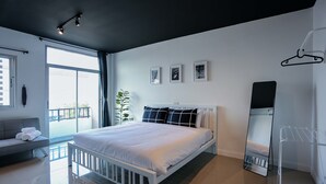 Un dormitorio moderno con una cama blanca, un sofá gris, un ventanal grande y un balcón.
