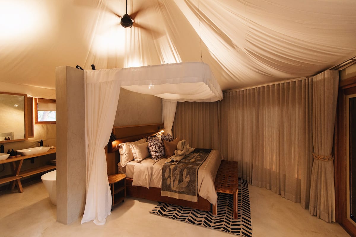 Een slaapkamer met een hemelbed, een houten bankje, een vloerkleed met een zebraprint en een grote spiegel.