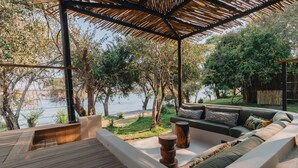 Un espacio de estar al aire libre cubierto con una terraza de madera, un sofá con cojines y vista a un cuerpo de agua.