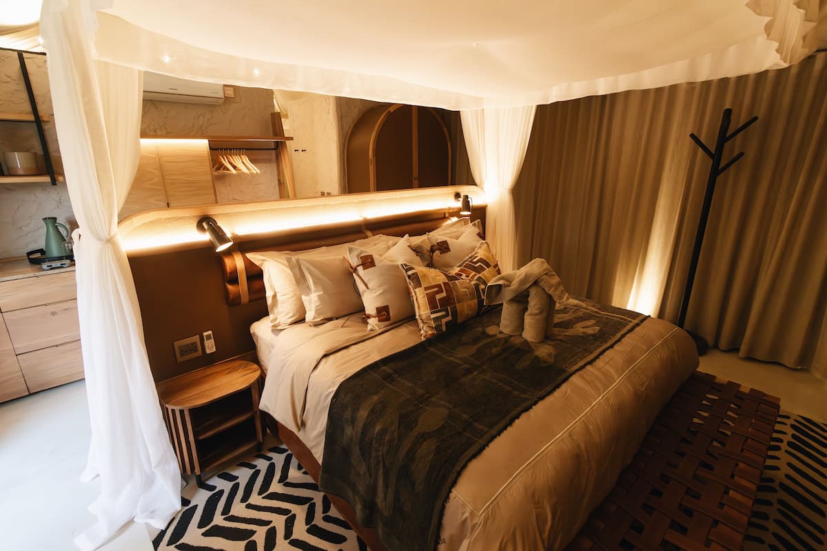 Een slaapkamer met een hemelbed, nachtkastjes, een spiegel en een kledingkast.