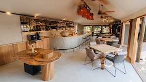 Zona de bar moderna con mostrador de mármol, sillas de madera y un ventilador de techo.