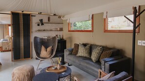 Amplia habitación con toldo, que incluye un sofá, sillas, una mesa de centro y ventiladores de techo.