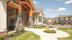 A modern apartment building with a stone facade, wooden beams, and a landscaped front yard.