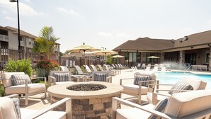 An outdoor pool area with lounge chairs, a fire pit, and umbrellas.