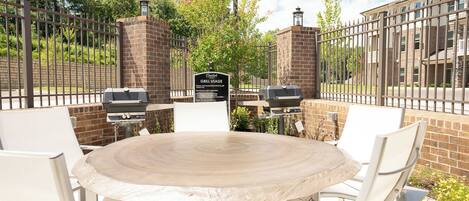 Un patio al aire libre con una mesa redonda y sillas blancas, rodeado por un muro de ladrillo y una valla de metal.
