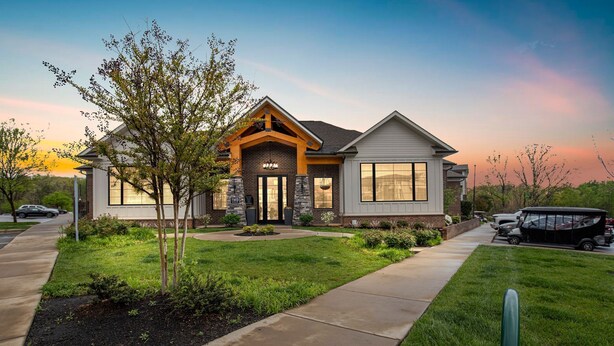 A modern two-story house with a stone facade, large windows, and a well-maintained lawn.