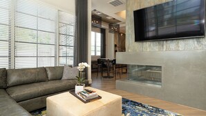 A modern living room with a sectional sofa, a coffee table with books, a fireplace, and a TV mounted on the wall.