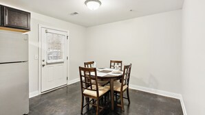 A dining area with a round table, four chairs, and a white door with a bulletin board.