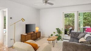 Una sala de estar moderna con un sofá, una mesa de centro, un televisor sobre un mueble de madera y una lámpara de pie.