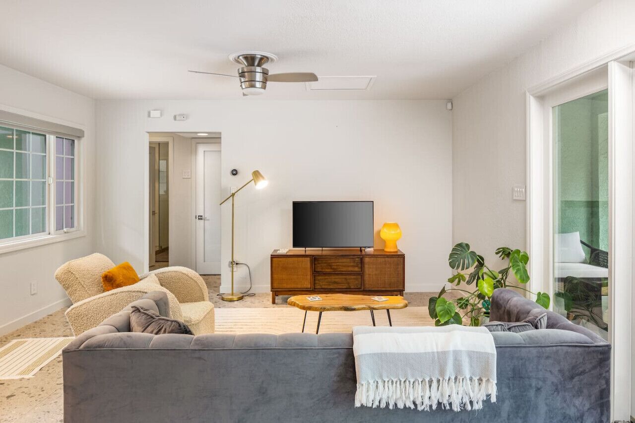 A modern living room with a grey sofa, a wooden coffee table, a television on a wooden cabinet, and a ceiling fan.