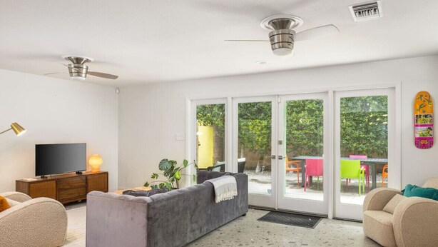 Una sala moderna con un sofá gris, un televisor y un ventilador de techo.