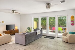A modern living room with a grey sofa, a TV, and a ceiling fan. - Olancha Palms - Private Pool and Spa! (Palm Springs)