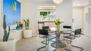 Een moderne eetruimte met een ronde glazen tafel, metalen stoelen en een vaas met bloemen.