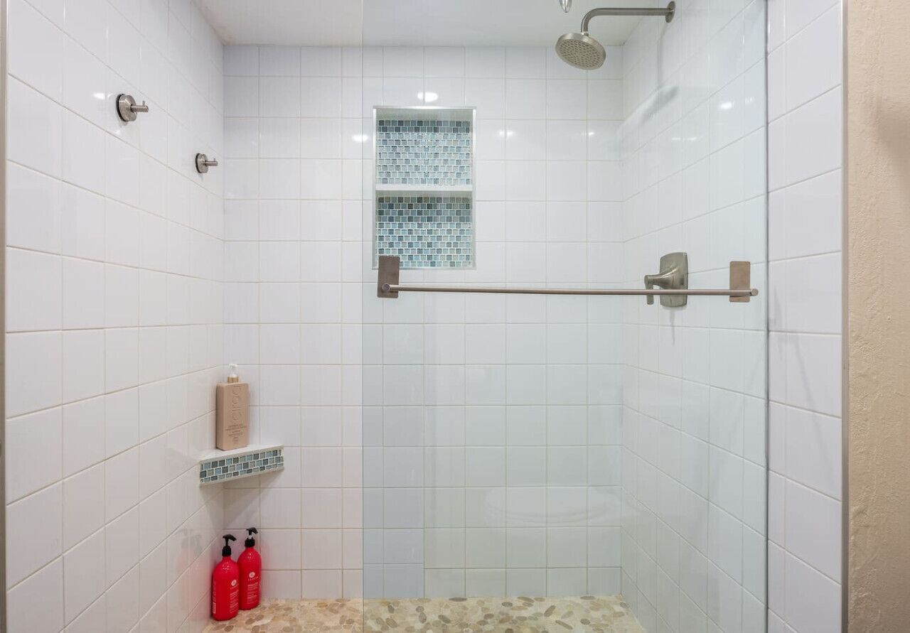 Une douche aux carreaux blancs, une fenêtre fermée par une paroi de verre et un porte-serviettes en métal.