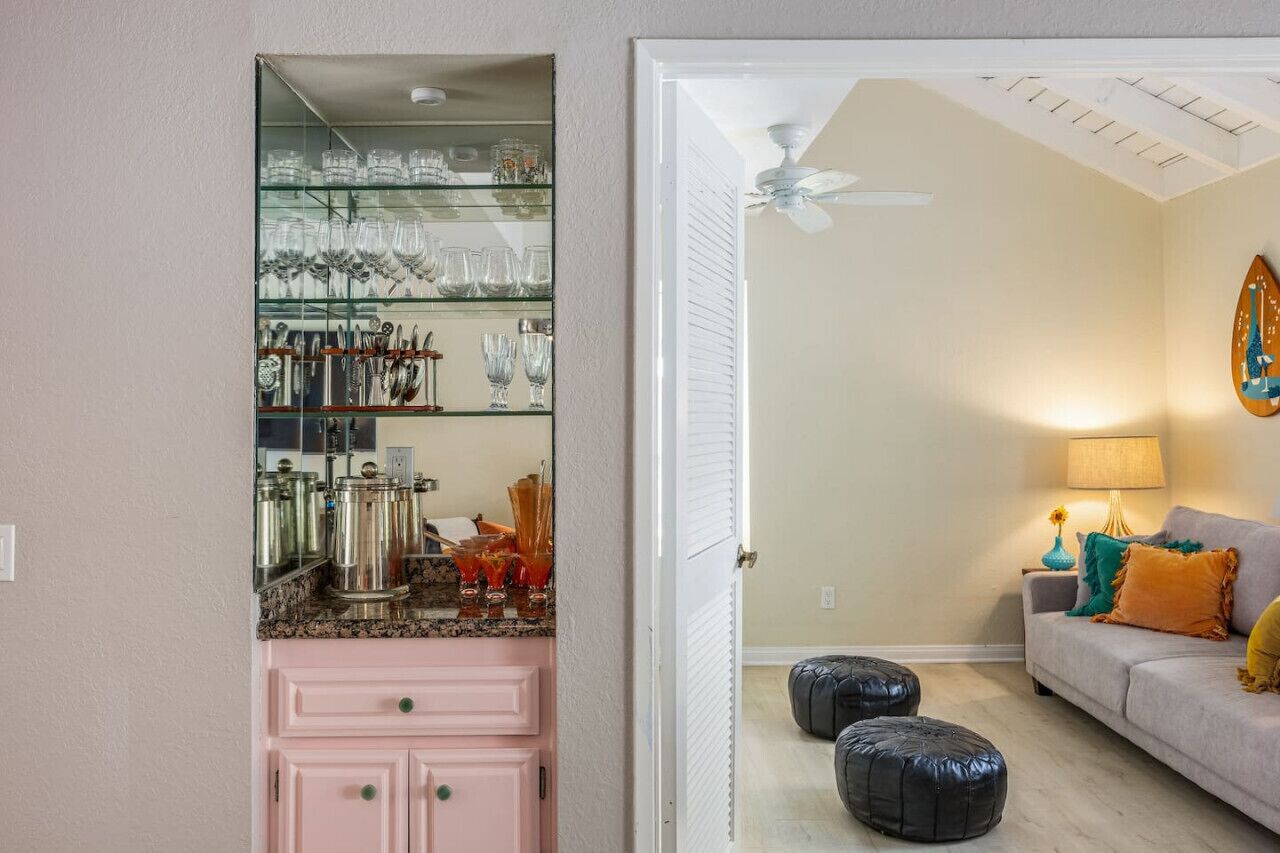 Ein Zimmer mit einem rosa Schrank, einer Glasvitrine, einem Deckenventilator, einem Sofa und einer Lampe.