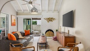 Een moderne woonkamer met een open haard, een plafondventilator en een flatscreen televisie aan de muur.