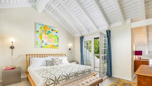Een slaapkamer met een bed, een bankje, een nachtkastje, een lamp en kunstwerken.