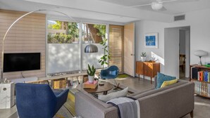 A modern living room with a flat-screen TV, a sofa, a blue chair, a coffee table, and a bookshelf. - MidMod Racquet Club Villa (Palm Springs)