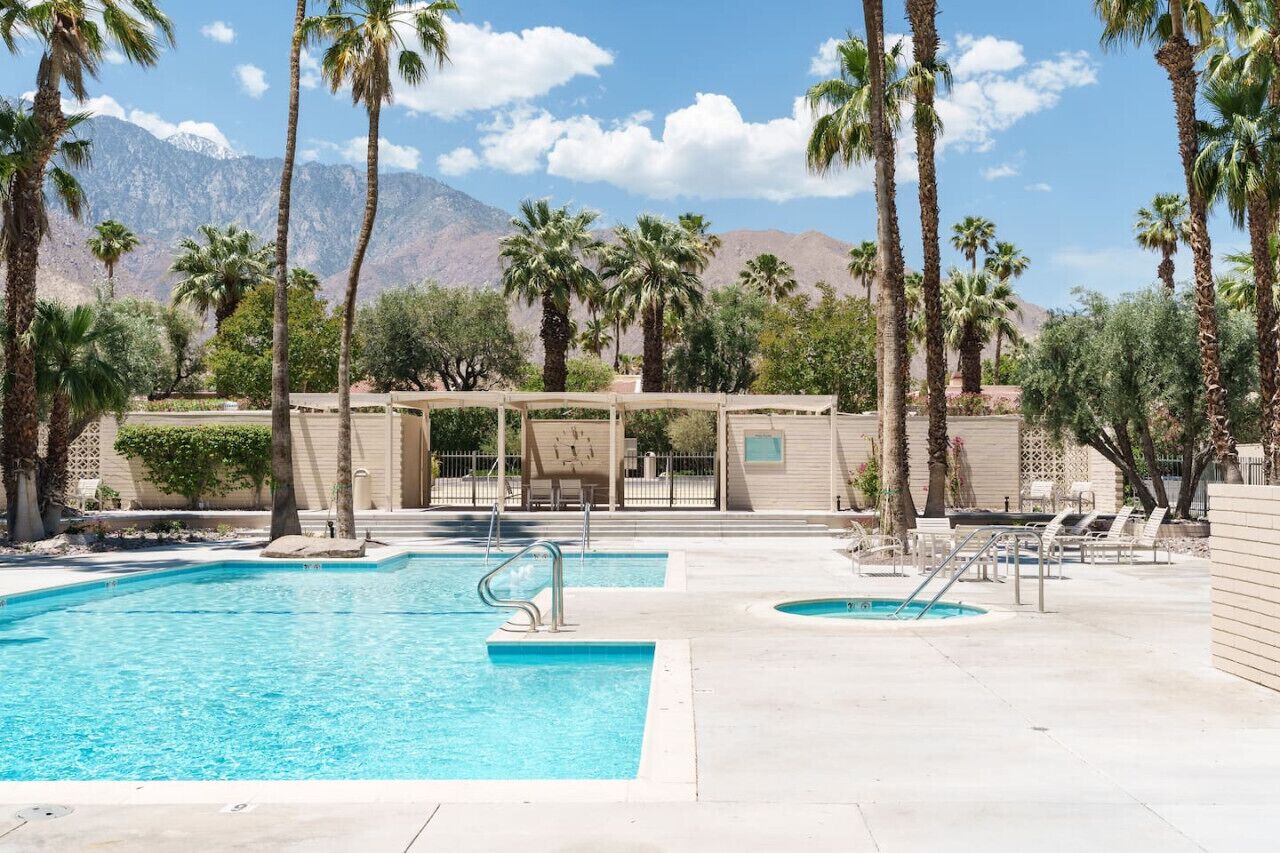 A pool area with two swimming pools, palm trees, and a building with a covered seating area.