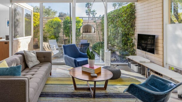 A modern living room with a sofa, blue armchair, and a coffee table with books. - MidMod Racquet Club Villa (Palm Springs)