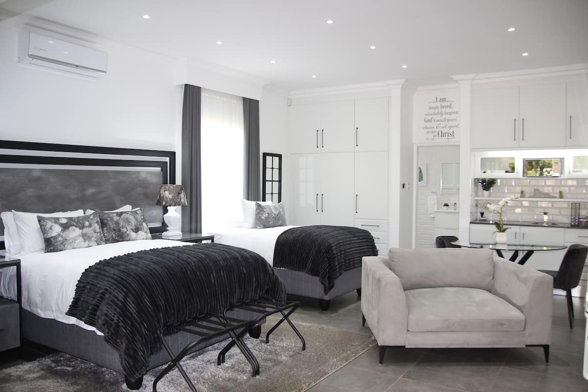 Un dormitorio moderno con dos camas, un sofá gris y una zona de cocina.