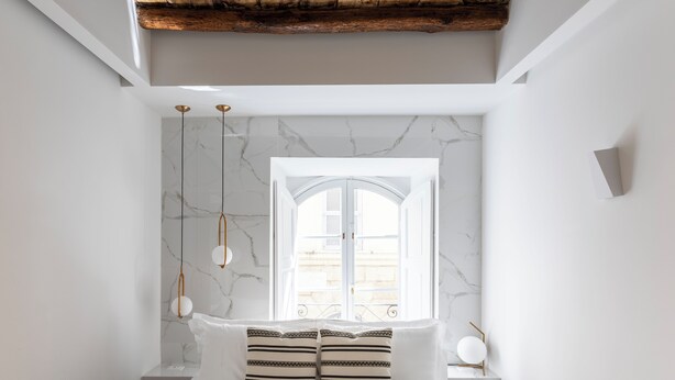 A bedroom with a bed, two bedside tables, a window with a view, and a wooden ceiling beam. - Louly Trevi Fountain 4 Bedroom Luxury Apartment (Roma)