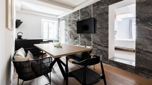 A modern dining area with a wooden table, black chairs, a TV mounted on a marble wall, and a view of a bathroom through an open doorway. - Louly Trevi Fountain 4 Bedroom Luxury Apartment (Roma)