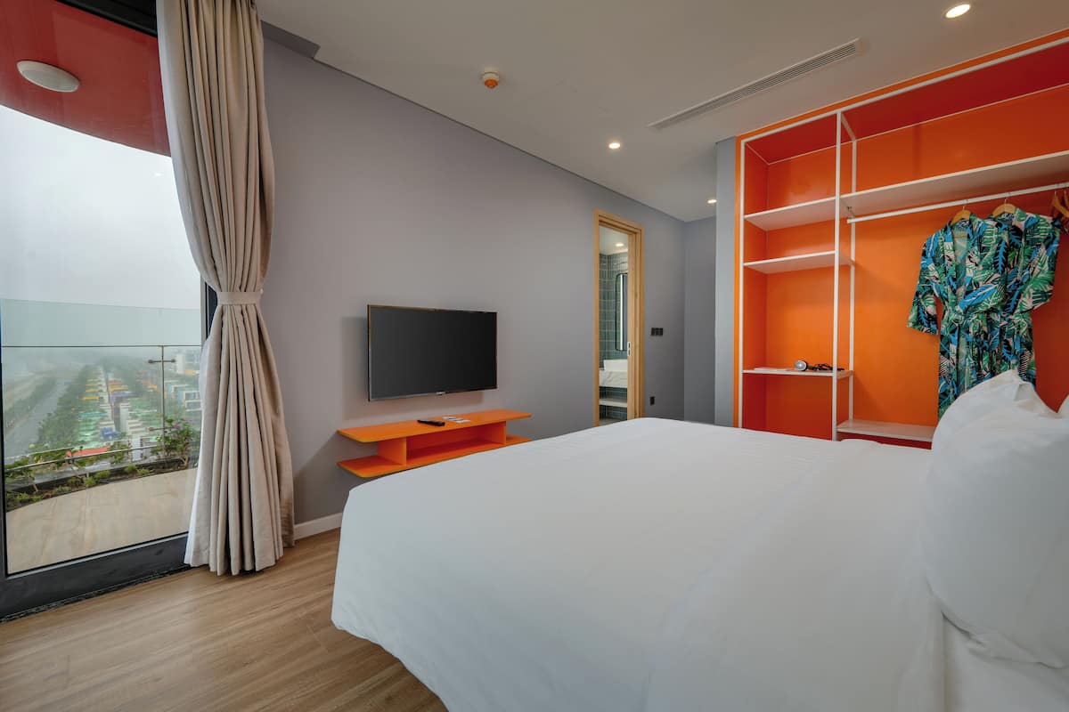 Une chambre d’hôtel avec un grand lit, une télévision, un balcon avec vue et un meuble de rangement orange.