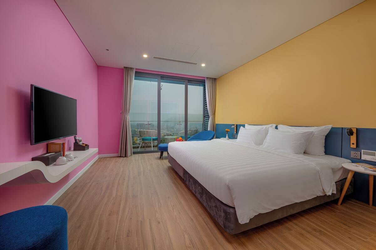 Une chambre d’hôtel moderne dotée d’un grand lit, d’une télévision à écran plat, d’un balcon avec vue et d’un plancher en bois.