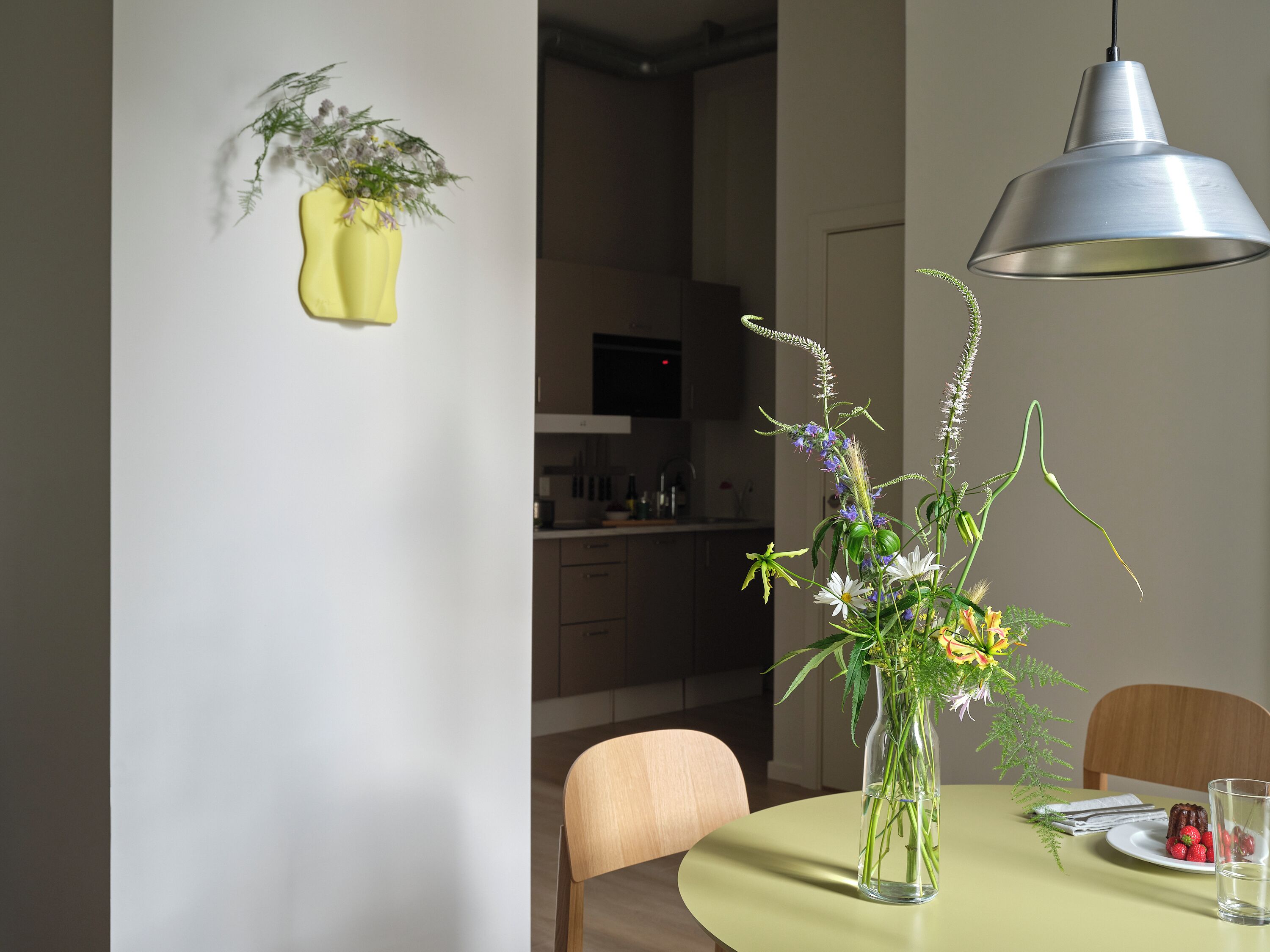 Un coin repas avec une table dressée pour deux personnes, un vase rempli de fleurs et un luminaire suspendu.