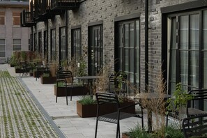 Una fila de mesas y sillas al aire libre, un edificio de ladrillo con amplios ventanales y un sendero pavimentado.