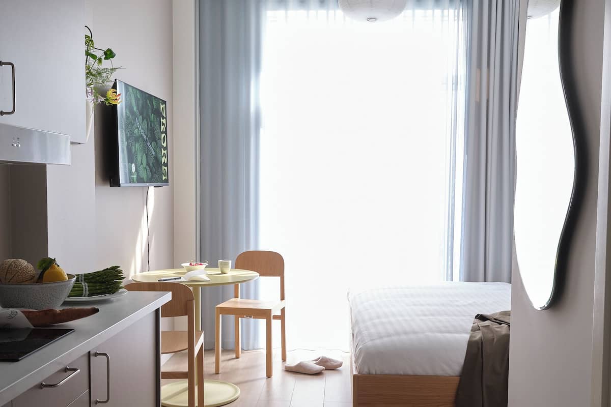 Quarto moderno e bem iluminado, com cama, mesa de cabeceira e um espelho grande.