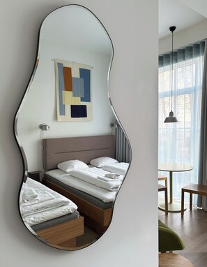 Un dormitorio moderno con un espejo único, una cama con sábanas blancas impecables, una obra de arte abstracta y colorida en la pared, y vistas del exterior a través de un ventanal grande.