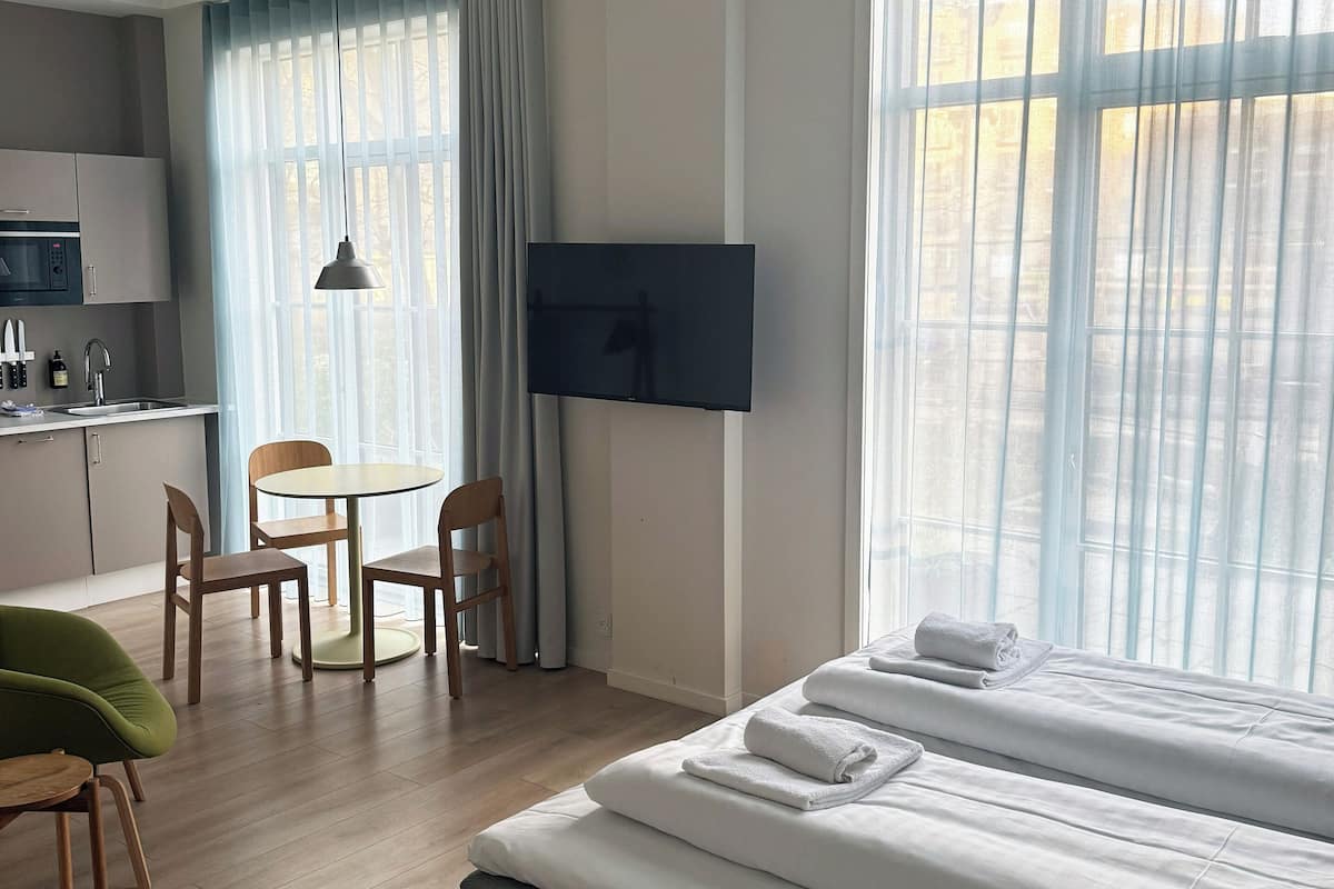 Quarto de hotel moderno com cama, televisão, área de refeições e cozinha.