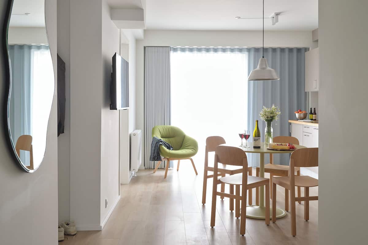 Uma área de jantar moderna com uma mesa posta para dois, uma cadeira verde e uma mesa de jantar de madeira.