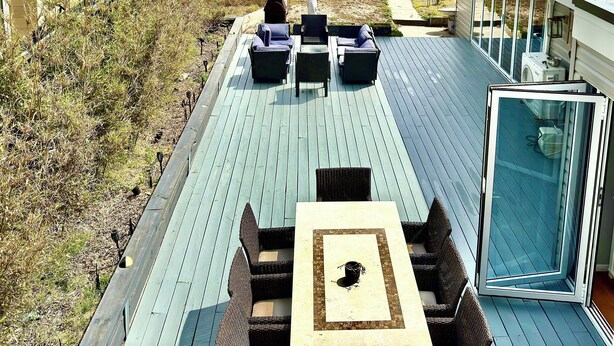 Eine Terrasse mit Gartenmöbeln, einer Glastür und Blick auf den Ozean.