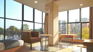 A hotel room with a bed, a chair, a small table, and a large window offering a city view. - Hotel Shivlok (Ujjain)
