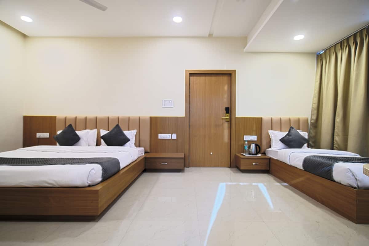 A hotel room with two beds, wooden headboards, a wooden door, a nightstand with a lamp, and a window with curtains.