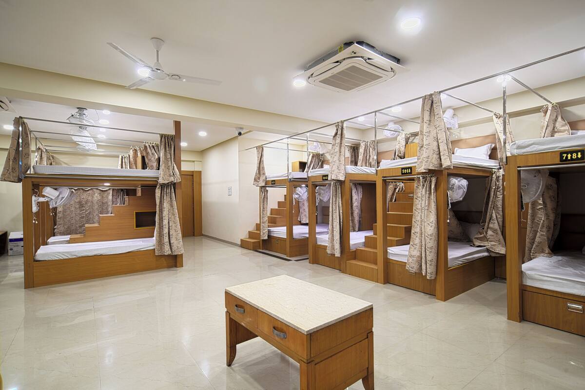 A dormitory room with bunk beds, a desk, and a ceiling fan.