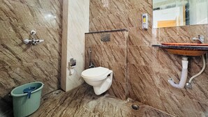A bathroom with a marble wall, a white toilet, a sink with a wooden basin, and a shower area. - Hotel Shivlok (Ujjain)