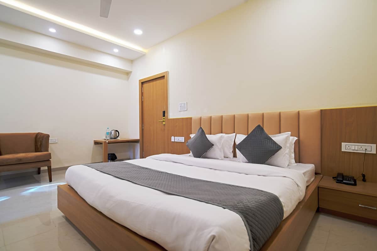 A hotel room with a large bed, a wooden headboard, a bedside table with a lamp, and a chair.