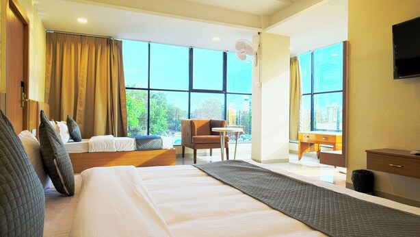 A hotel room with a large bed, a sitting area with a chair and table, a small desk, and a TV mounted on the wall. - Hotel Shivlok (Ujjain)