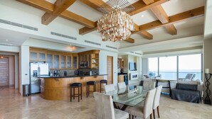 A spacious kitchen with a central island, wooden beams, and a large window overlooking the ocean. - Ocean Wrap Around Oceanfront Balcony at Tessoro (Las Conchas)