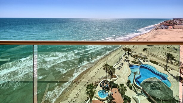 A beachfront view from a balcony with a pool, palm trees, and a beach area. - Ocean Wrap Around Oceanfront Balcony at Tessoro (Las Conchas)